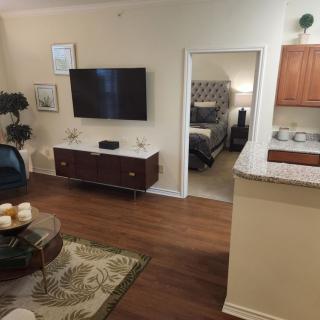 A cozy living space featuring a wall-mounted television, stylish furniture, and an open view into a bedroom and kitchen.