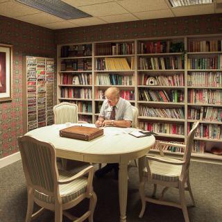A person reading at a table in a cozy library setting surrounded by bookshelves.