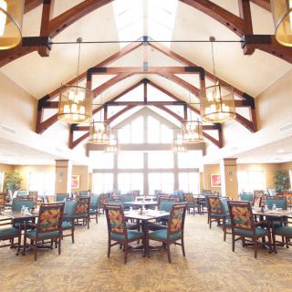 A spacious dining area with elegant wooden beams and large windows, featuring neatly arranged tables and chairs.