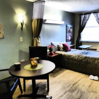 A cozy studio apartment with a comfortable bed, small dining table, and ample natural light from the window.