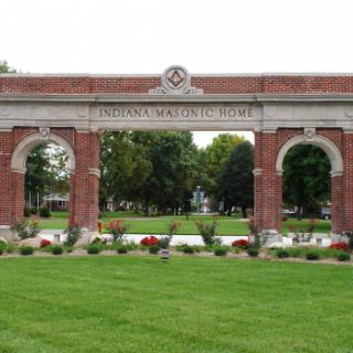 A large brick archway in a park setting with green grass and flowers.