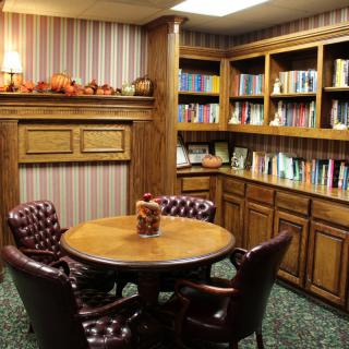 A cozy library corner with a round table surrounded by chairs and bookshelves filled with books.