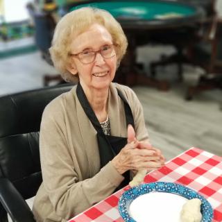 An elderly woman sitting at a table with a checkered tablecloth, preparing to dine.