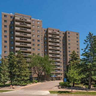 A tall residential apartment building surrounded by trees under a clear blue sky.