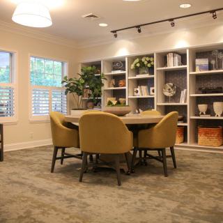 A modern meeting room with a round table and comfortable chairs surrounded by bookshelves and decor.