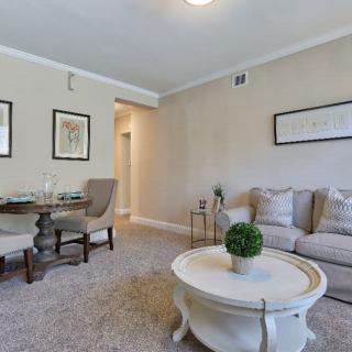 A cozy living room with a neutral color palette featuring a comfortable sofa and a round coffee table, complemented by a small dining area in the corner.