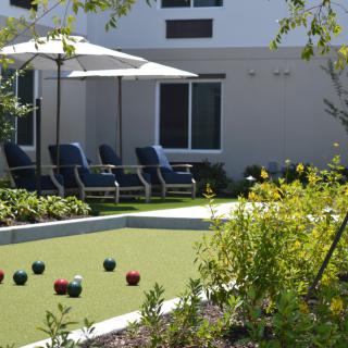 A serene outdoor space featuring a bocce court surrounded by lush greenery, complete with lounge chairs and umbrellas for relaxation.