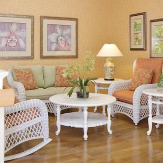 A cozy living room with rattan furniture, featuring a sofa and chairs, a round coffee table, decorative wall art, and an indoor plant.