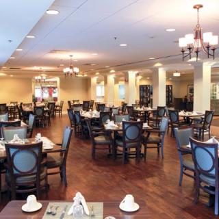 An elegantly furnished restaurant dining room with neatly arranged tables and chairs, featuring warm lighting.