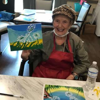 An elderly person happily displaying a painting during an art activity.