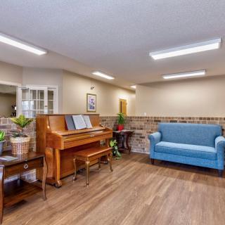 A cozy room with a piano and a blue couch, decorated with plants and featuring bright lighting.