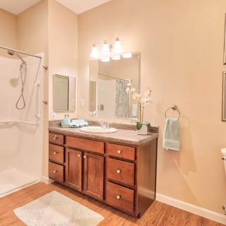 A well-lit bathroom with a wooden vanity, large mirror, and walk-in shower.