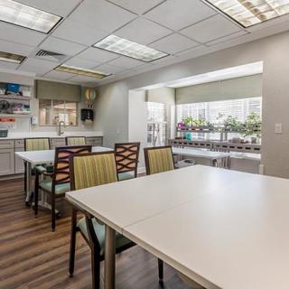 A spacious and well-lit community room with tables, chairs, and a kitchenette.