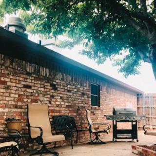 A cozy backyard patio with seating and a grill under a tree.