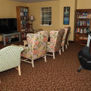 A cozy living room with floral armchairs, a large television, and filled bookshelves.
