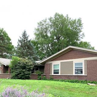 A suburban brick house with a well-maintained front yard and surrounding trees.