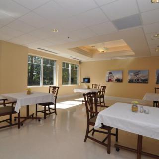 A modern dining room with several tables and chairs, illuminated by natural daylight through large windows.