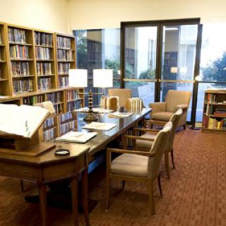 A quiet study room in a library, featuring bookshelves, a table with chairs, and ample lighting.
