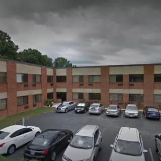 A two-story brick building with a parking lot filled with cars under a cloudy sky.