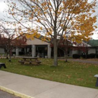 A view of a building surrounded by trees with autumn foliage, featuring picnic tables and a sidewalk.