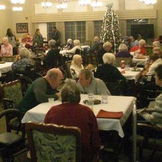 A group of elderly people gathered in a dining room decorated with a Christmas tree.