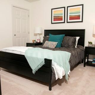 A cozy bedroom with a modern design, featuring a dark bed frame, colorful throw pillows, and abstract artwork on the walls.