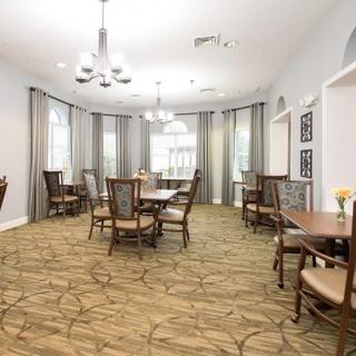 A bright and elegant dining room with multiple tables and chairs, overhung by chandeliers.