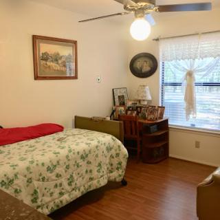 A cozy bedroom featuring a bed with floral bedding, a wooden desk, and a window allowing natural light to fill the space.