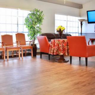 A bright and cozy living room with orange chairs, a small table, and a television mounted on the wall.