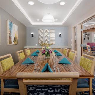 A modern dining room with a well-set table, adorned with teal napkins and floral centerpieces.