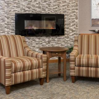 A cozy living room setting with two striped armchairs flanking a small side table, set in front of a modern fireplace.