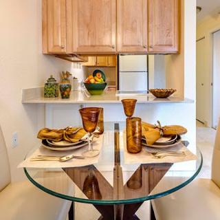 A beautifully arranged dining area featuring a glass table set for a meal, complemented by wooden kitchen cabinets and decorative items.