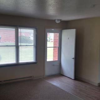 An empty room with a window and open door allowing natural light.