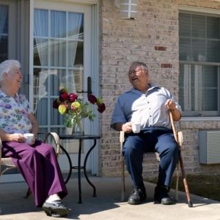 Two seniors enjoying a conversation on a sunny patio.