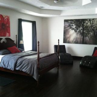 A modern bedroom with dark flooring, featuring a bed, two chairs, and artwork on the walls.