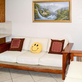 A cozy living room features a white sofa with a smiley face pillow and decorative cushions beneath a landscape painting.