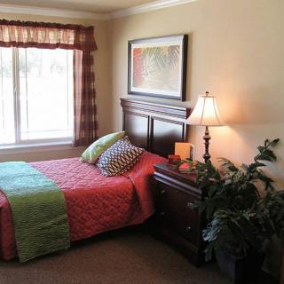 A cozy bedroom with a single bed, vibrant bedding, and a bedside lamp near the window.