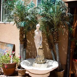 A decorative garden fountain with a statue surrounded by palm trees and potted plants.