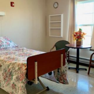 A well-lit hospital room with a single bed, chair, and flowers by the window.