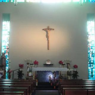 A serene church interior featuring an altar with a crucifix and stained glass windows.