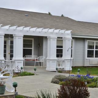 A suburban house with a white pergola over the front porch and landscaped front yard.