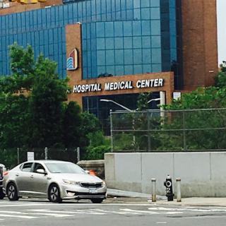 A view of a hospital medical center with a car parked nearby in an urban setting.