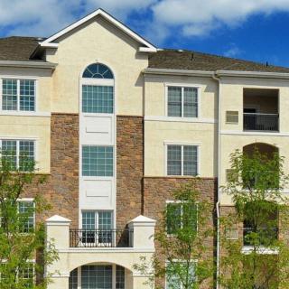 A modern apartment building with a brick and stucco facade, surrounded by trees under a blue sky.