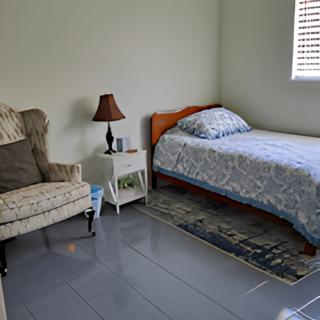A simple bedroom with a single bed, armchair, and nightstand.