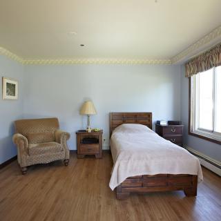 A minimalist bedroom with a single bed, armchair, and a large window.