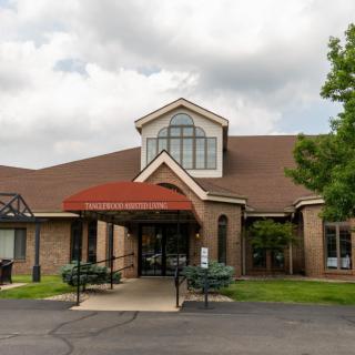A building with a red-roofed entrance and brick exterior under a cloudy sky, surrounded by trees.