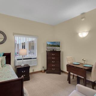 A cozy bedroom with a bed, dresser, and a small dining table set near a window.
