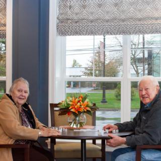 Two seniors sitting at a table in a cozy cafe, enjoying each other's company.