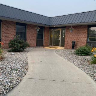 A welcoming entrance to a modern brick building surrounded by landscaped gardens and a concrete pathway.