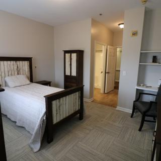 A minimalist bedroom with a single bed, wardrobe, and a small desk and chair.